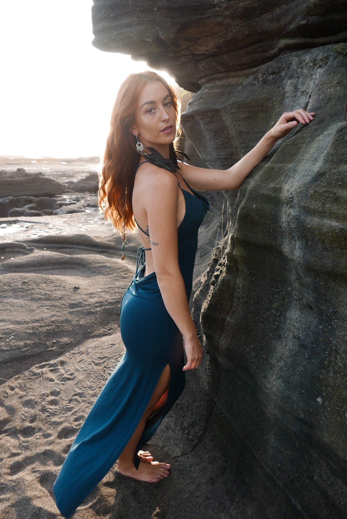 Beautiful dress with open back, side cuts and delicate strap details crossing the back in color dark teal.