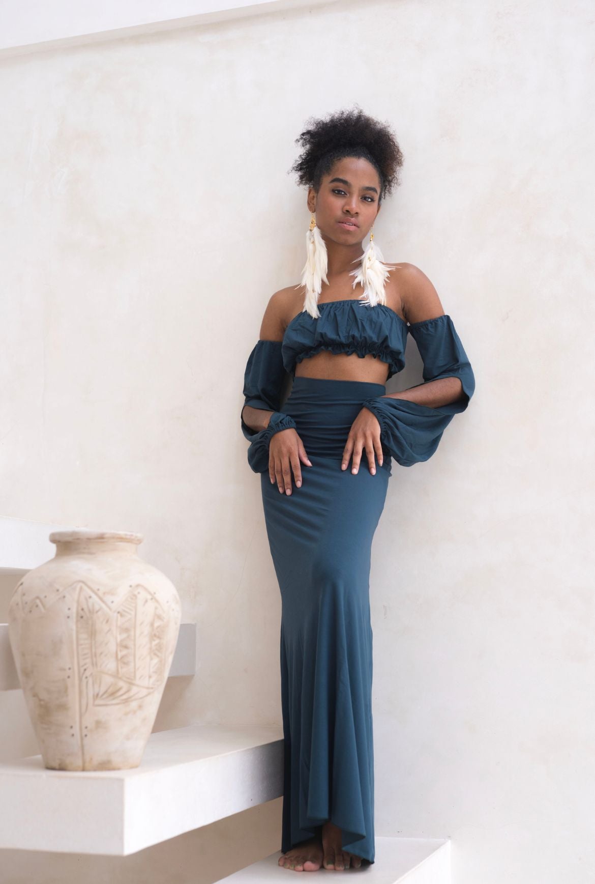 Model posing in Bohemian Goddess Liberate - Off shoulder puffy sleeve boho top and Enchanted high waist skirt with bow in the back in color dark teal