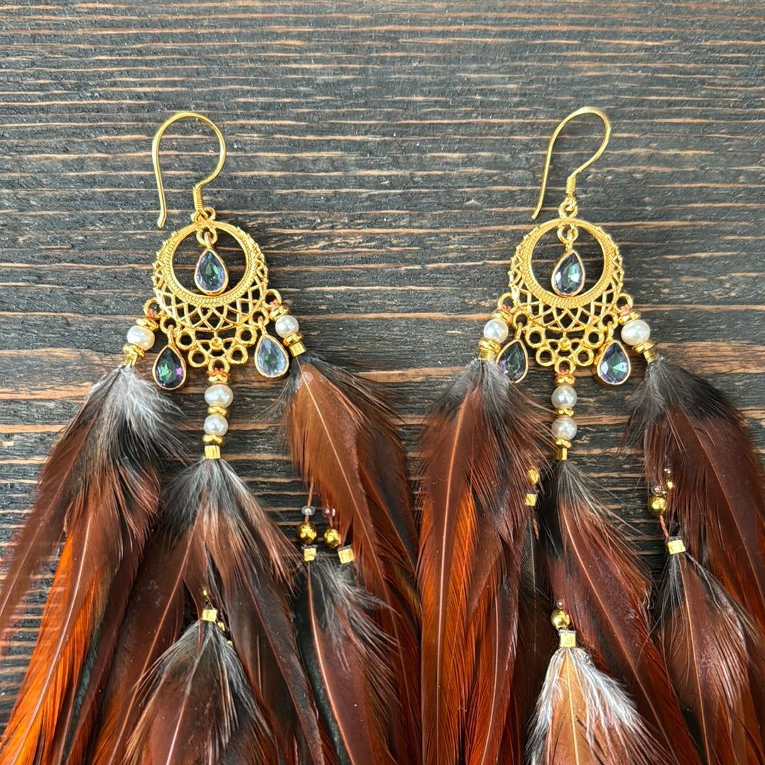 Close up view of Hecate feather earrings showing brown feathers, white and golden beads and gold plated moon chandelier.
